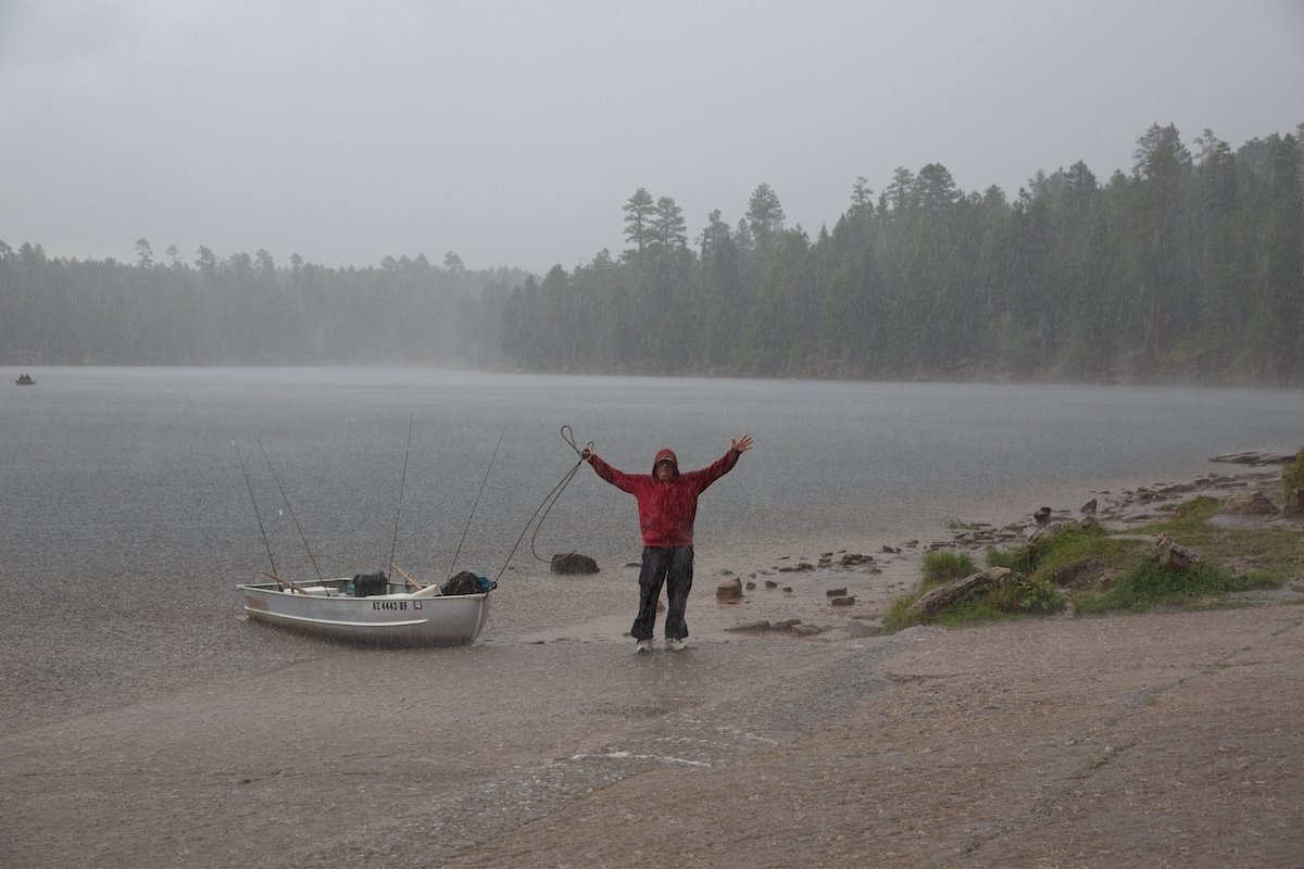 Unedited image of person posing with hands up beside a boat and lake in the rain